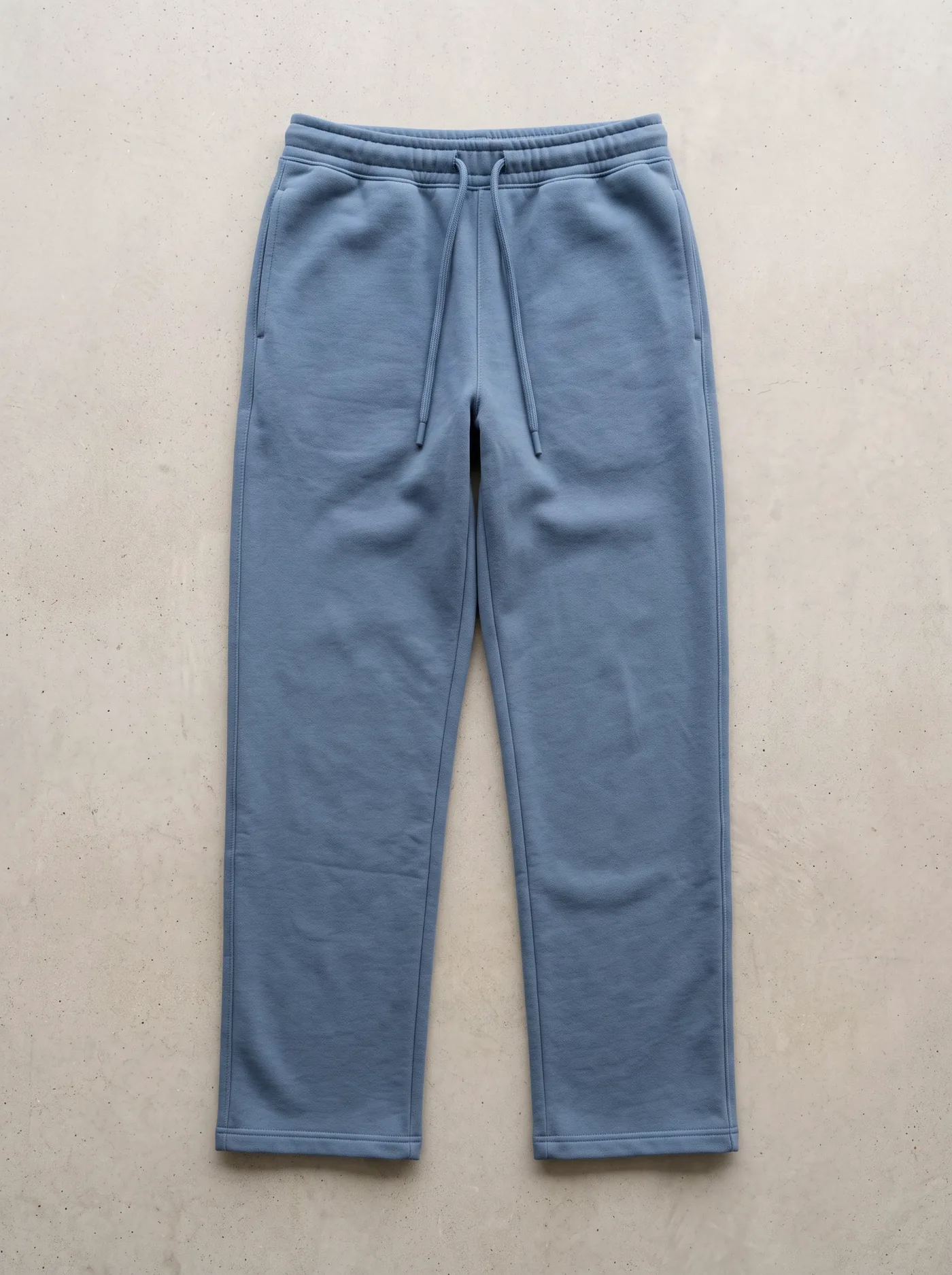 Plain steel-blue sweatpants laid flat on concrete